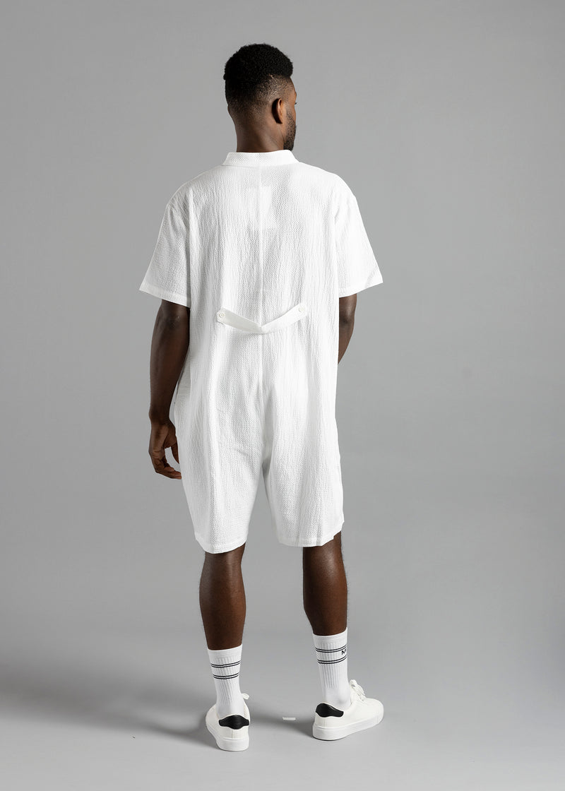 Rear view of the white MW Button Up Jumpsuit by MilkWhite on a model, showing the short sleeves and buttoned waist strap.