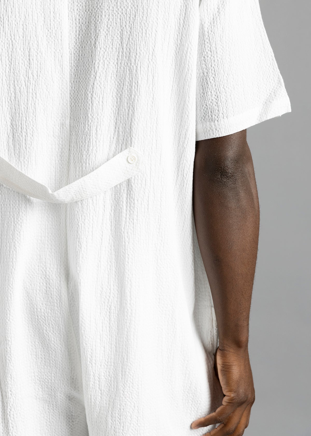 Rear close-up of the white MW Button Up Jumpsuit by MilkWhite, showing the buttoned waist strap and textured surface.