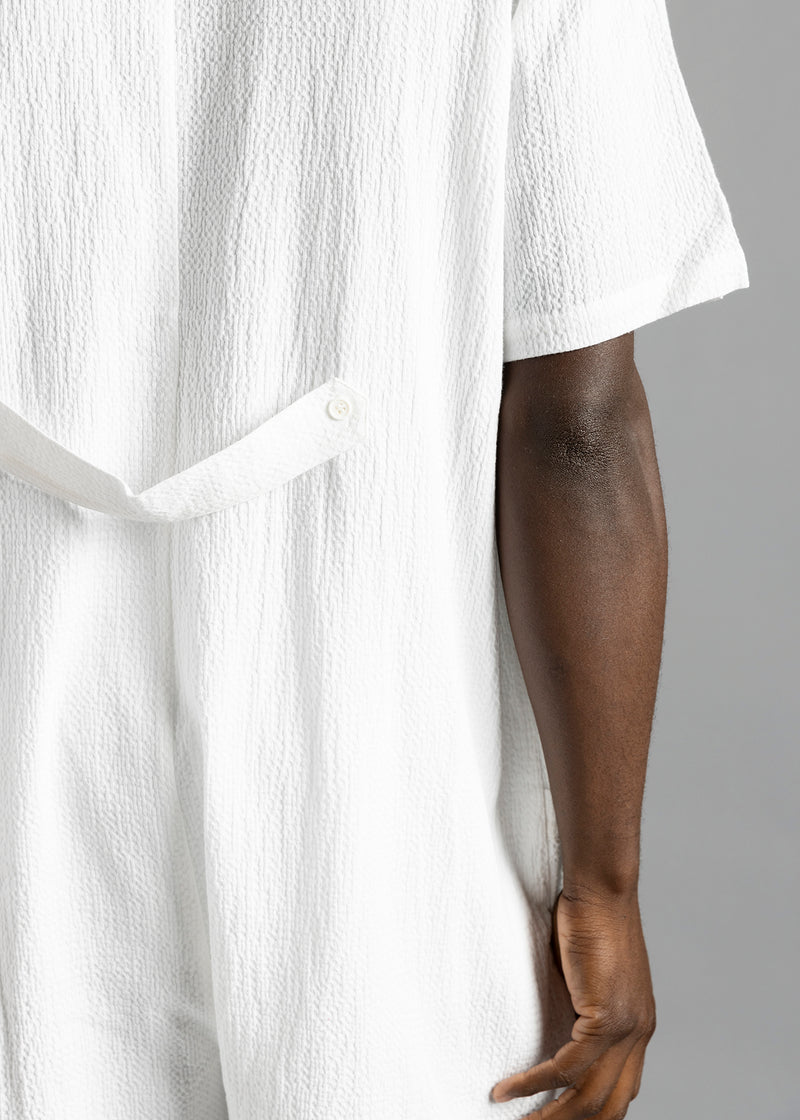 Rear close-up of the white MW Button Up Jumpsuit by MilkWhite, showing the buttoned waist strap and textured surface.