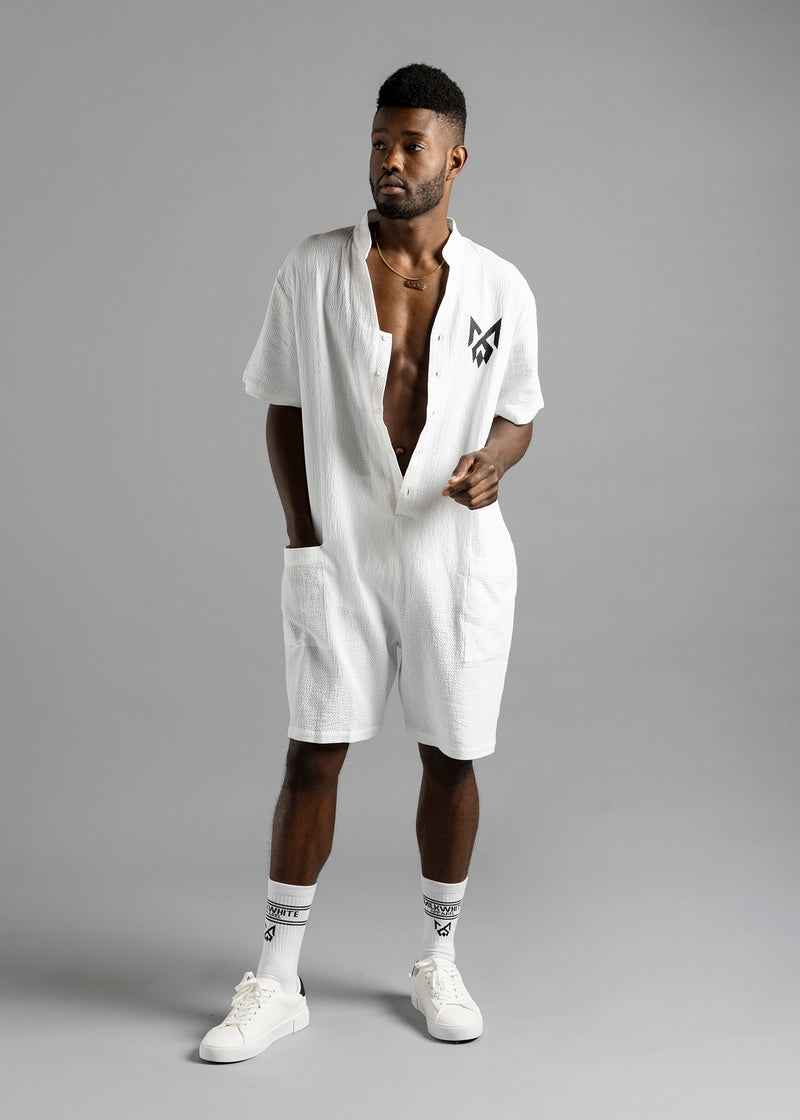 Front view of a model looking to the side in the white MW Button Up Jumpsuit by MilkWhite, showing its black chest logo.