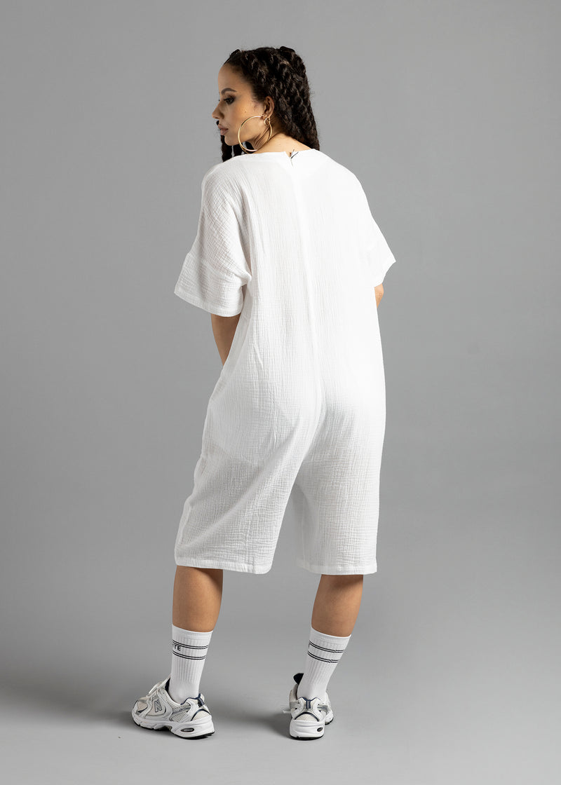 Full-length rear view of a model wearing the white MW V-Cut Jumpsuit by MilkWhite, showing its plain back, short sleeves and knee-length legs.