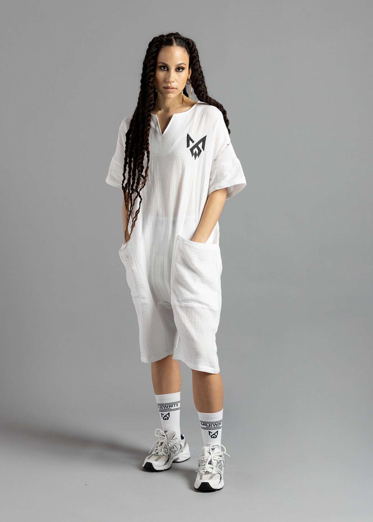 Full-length front view of a model wearing the white MW V-Cut Jumpsuit by MilkWhite with both hands in the large front pockets.