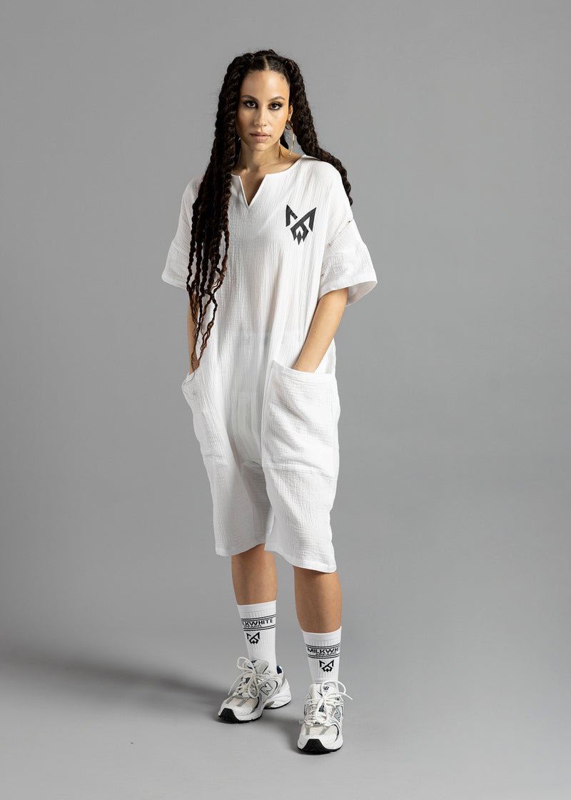 Full-length front view of a model wearing the white MW V-Cut Jumpsuit by MilkWhite with both hands in the large front pockets.