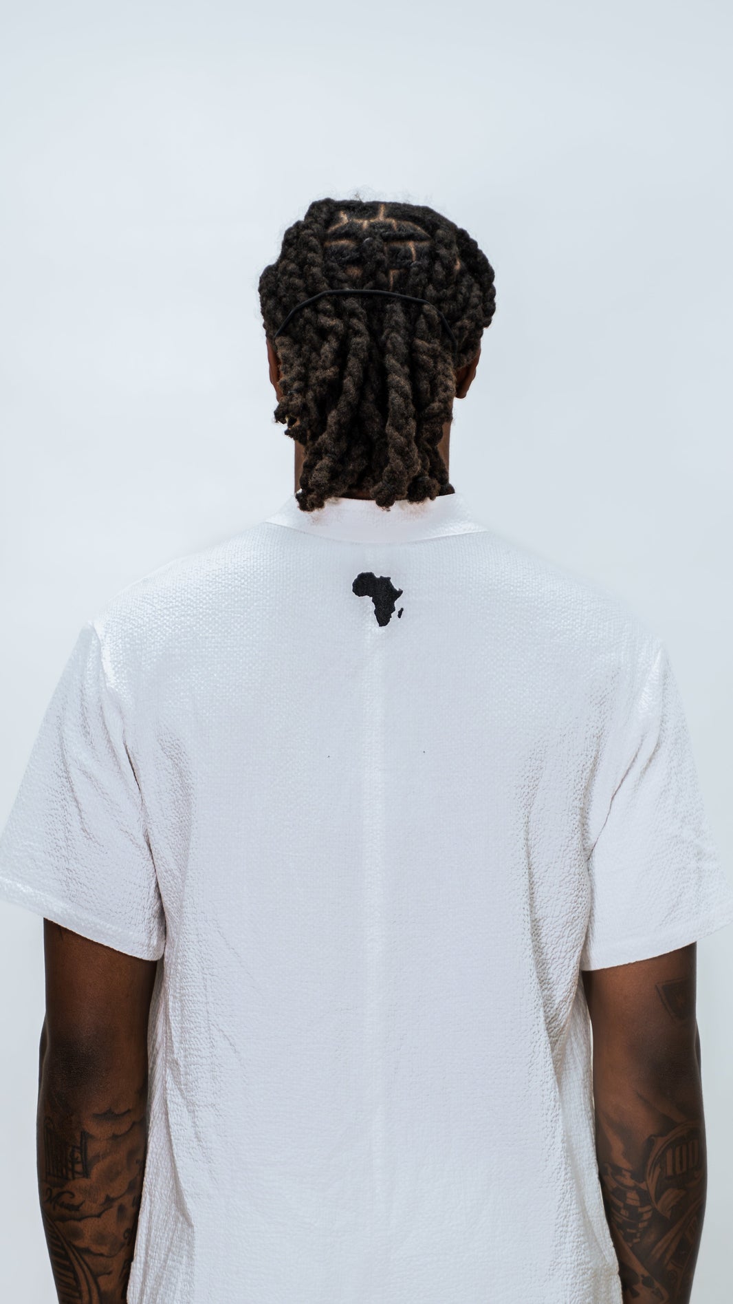 Person wearing a Milkwhite white jumpsuit with a black silhouette logo of africa near top of the neck.