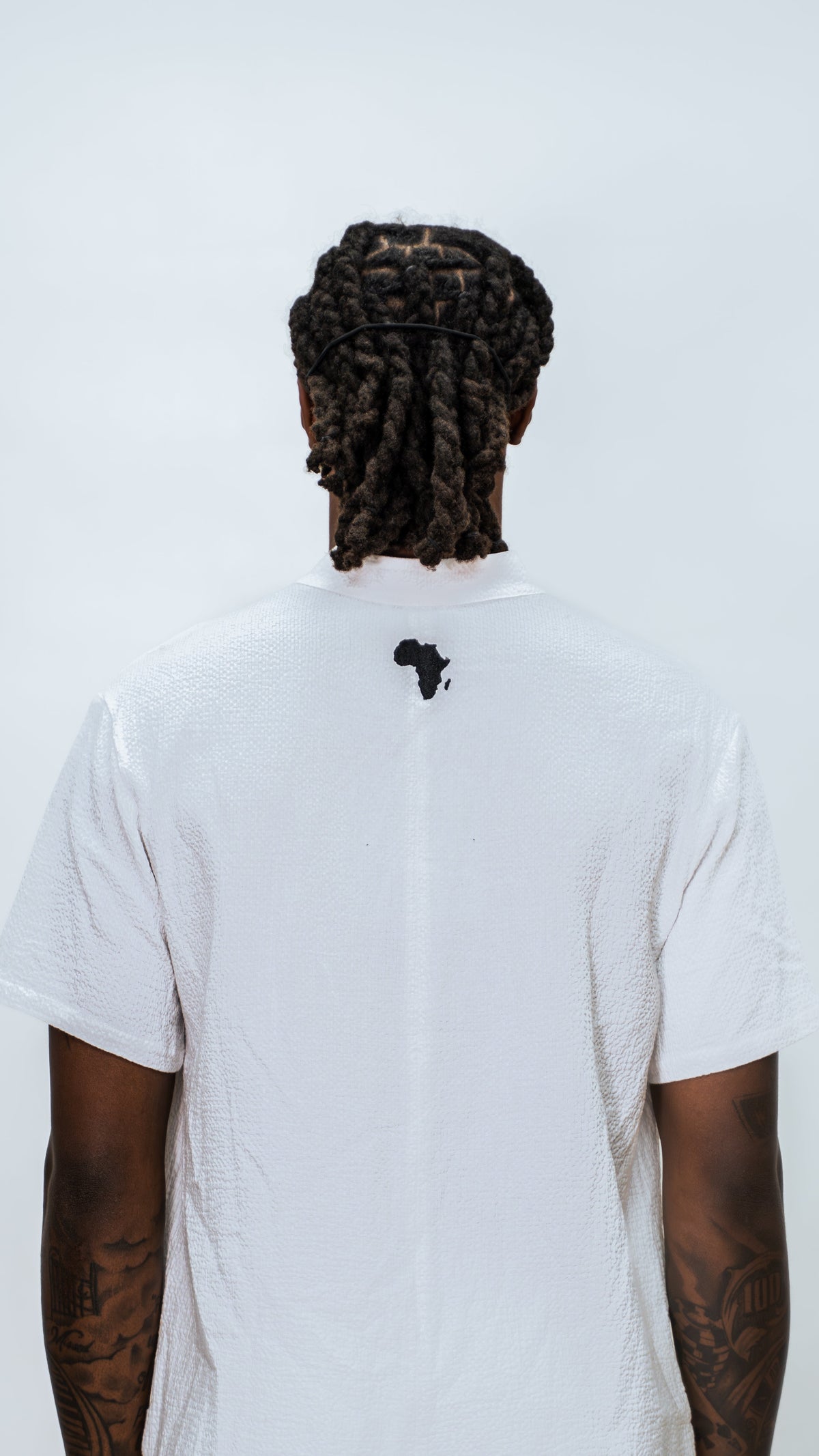 Person wearing a Milkwhite white jumpsuit with a black silhouette logo of africa near top of the neck.