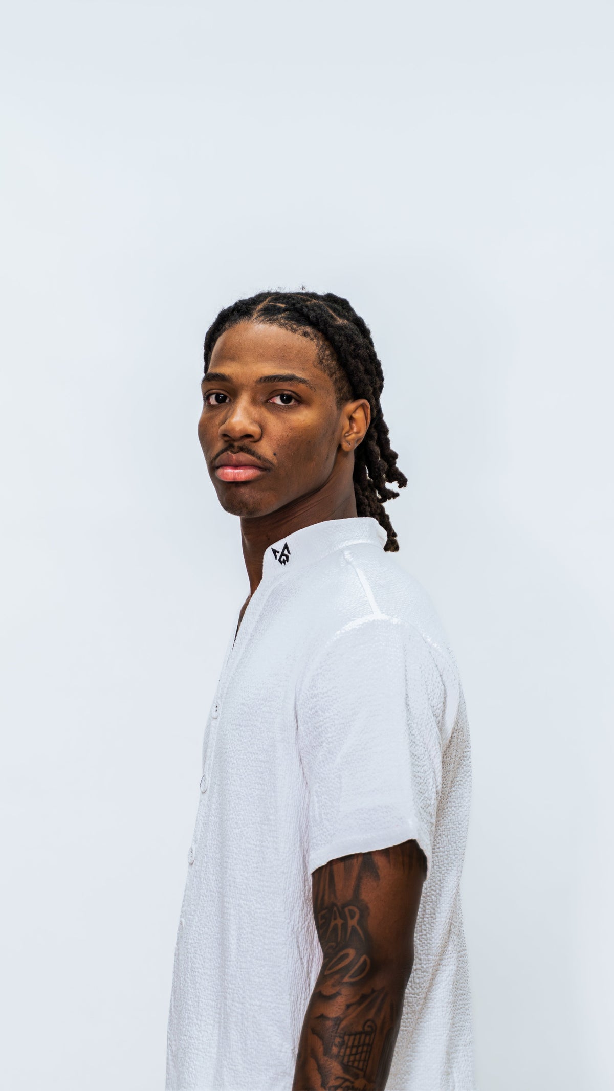 Side view of Person wearing a Milkwhite white button down jumpsuit with a black silhouette logo of africa on the collar.