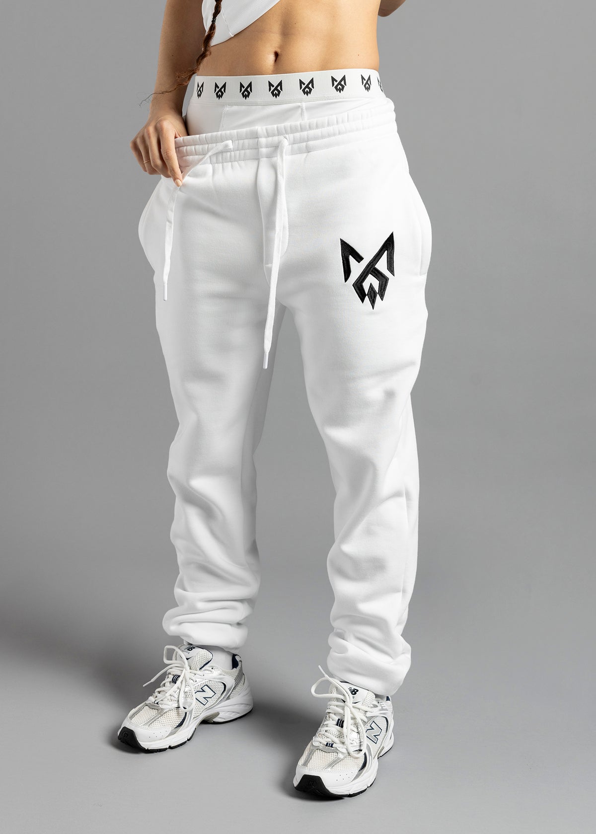 Front view of white MilkWhite Comfortable Joggers on a model, showing the drawstring waist, black thigh logo and gathered ankle cuffs.