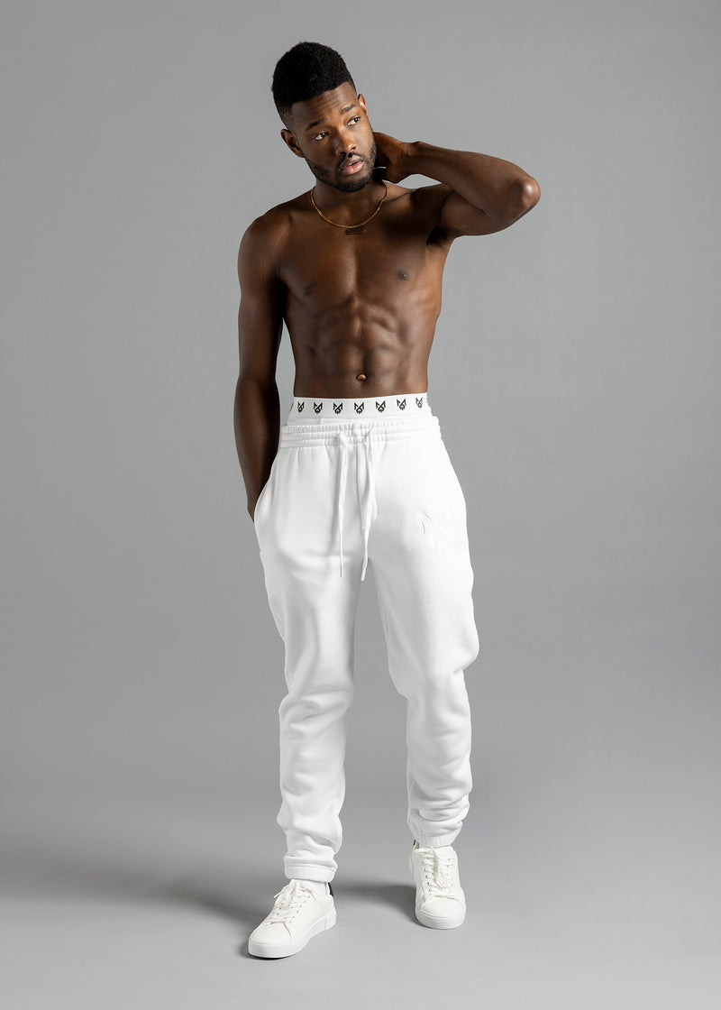 Full-length front view of a model wearing white MilkWhite Comfortable Joggers, with one hand behind the neck and the other in a side pocket.