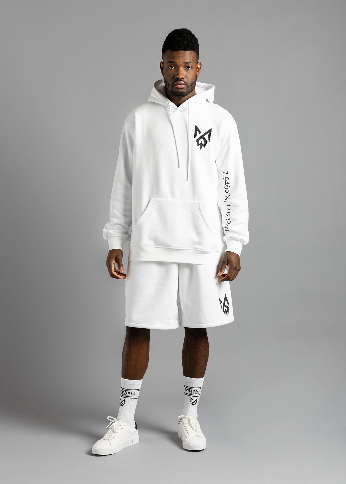 Model wearing an everyday premium MilkWhite white essential hoodie with sleeve ghana coordinate details and MW logo.