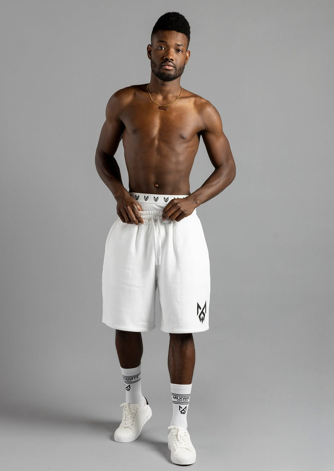 Front view of a model holding the waistband of MilkWhite Jogger Shorts, showing the relaxed fit and black leg logo.