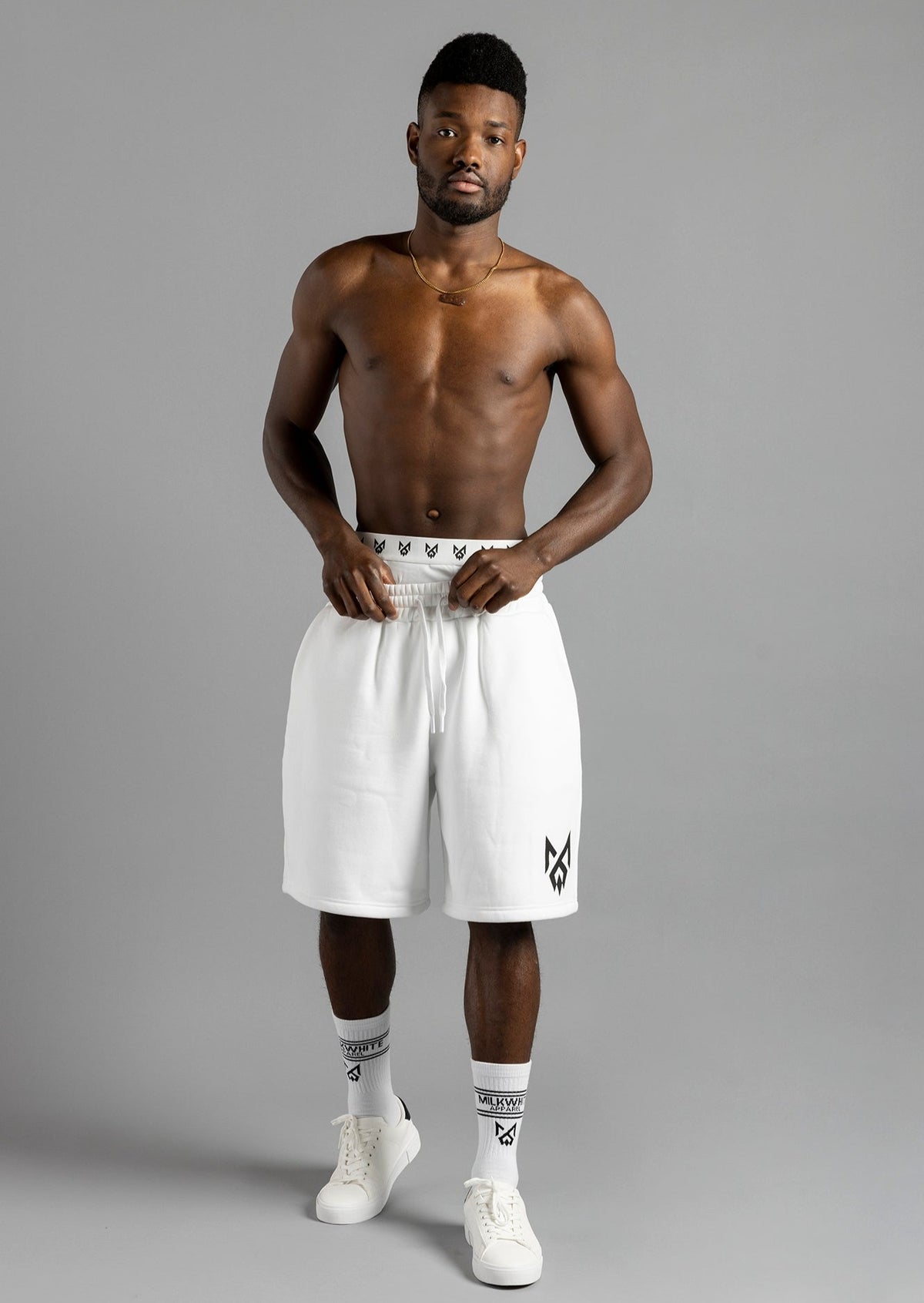 Front view of a model holding the waistband of MilkWhite Jogger Shorts, showing the relaxed fit and black leg logo.