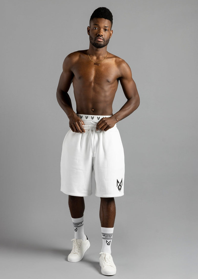 Front view of a model holding the waistband of MilkWhite Jogger Shorts, showing the relaxed fit and black leg logo.