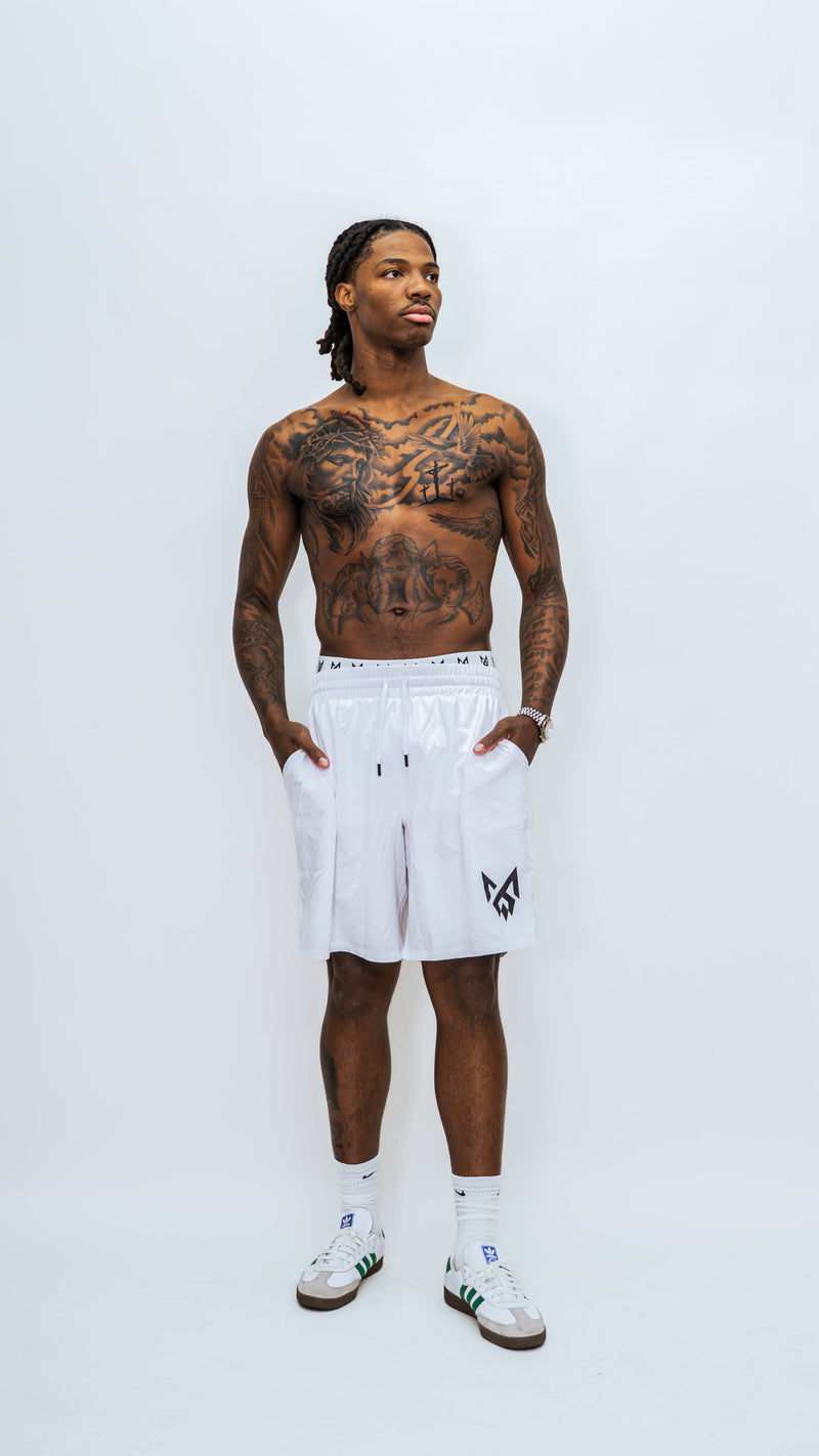 Model wearing white MilkWhite Long Swim Trunks in a full-length front view, with hands in the side pockets and a black leg logo.