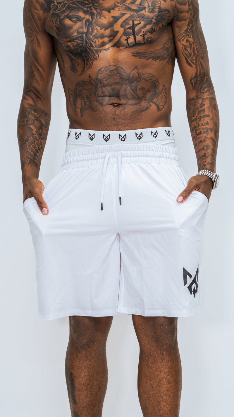 Front view of white MilkWhite Long Swim Trunks on a model with both hands in the pockets, showing the drawstring and black leg logo.