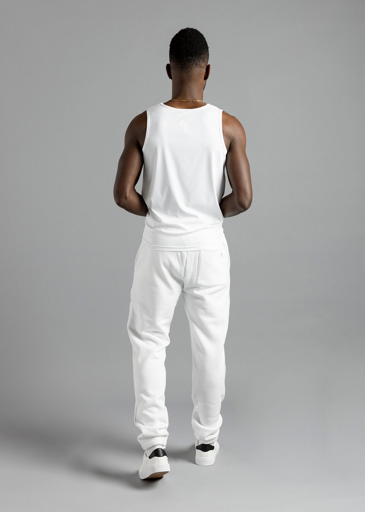 Full-length rear view of a model wearing the white MilkWhite Premium Tank Top with white joggers.