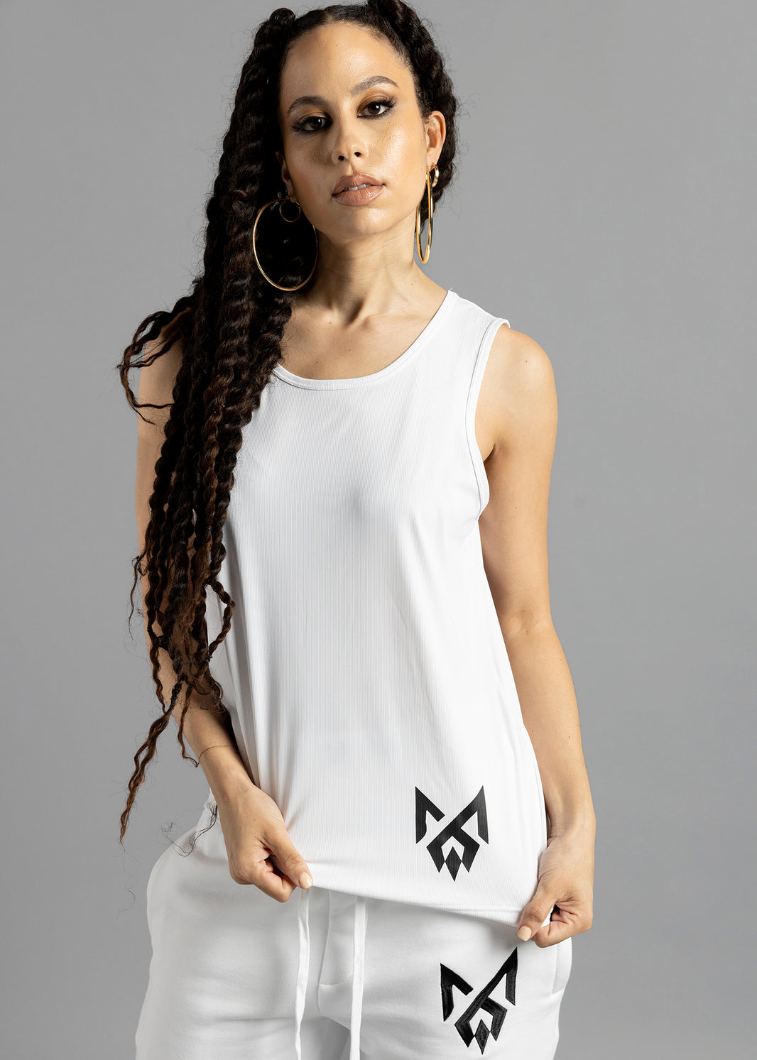 Front view of a model holding out the hem of the white MilkWhite Premium Tank Top, showing its scoop neckline and black logo.