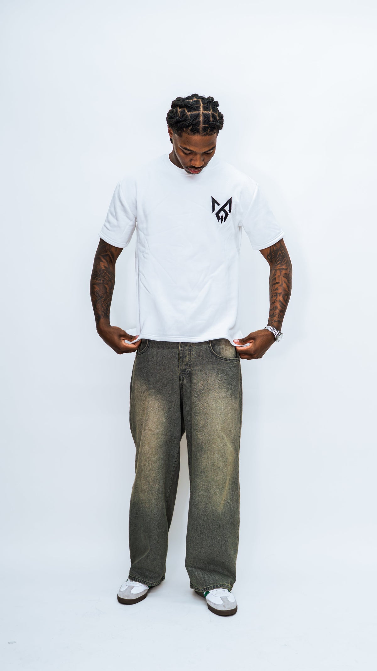 Front view of a model looking down and holding the hem of the white MilkWhite Short Sleeve Sweatshirt with a black chest logo.