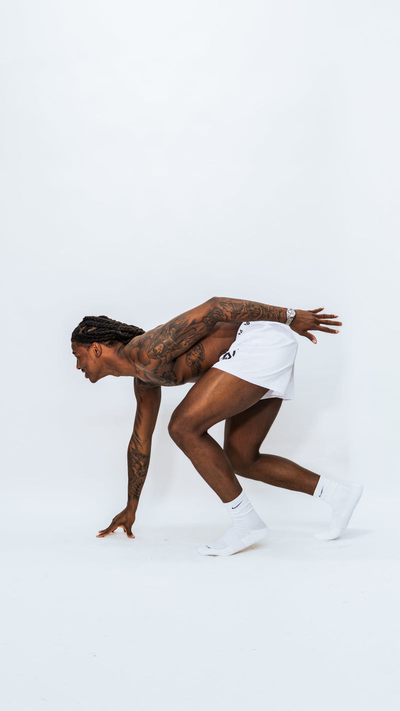 Model wearing Milkwhite Short swim trunks in an athletic sprint pose against white background. 