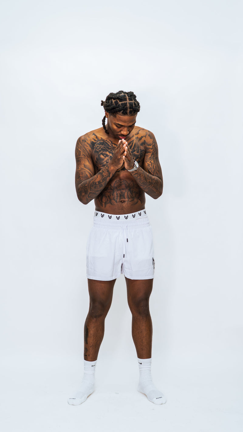 Male model wearing Milkwhite short white swim trunks against a white background.