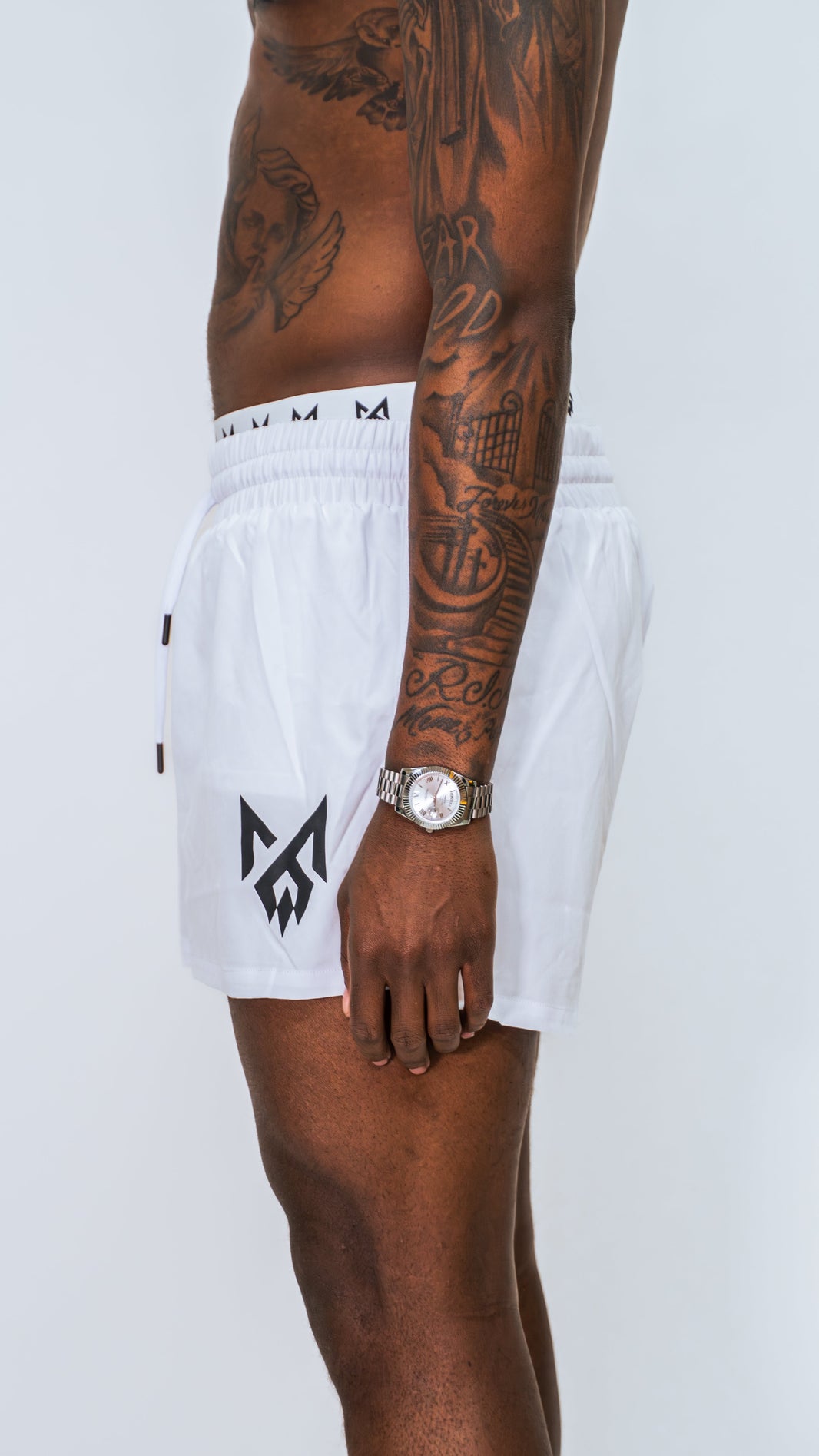 Male model wearing MilkWhite short swim trunks showing Milkwhite's logo on bottom left leg.