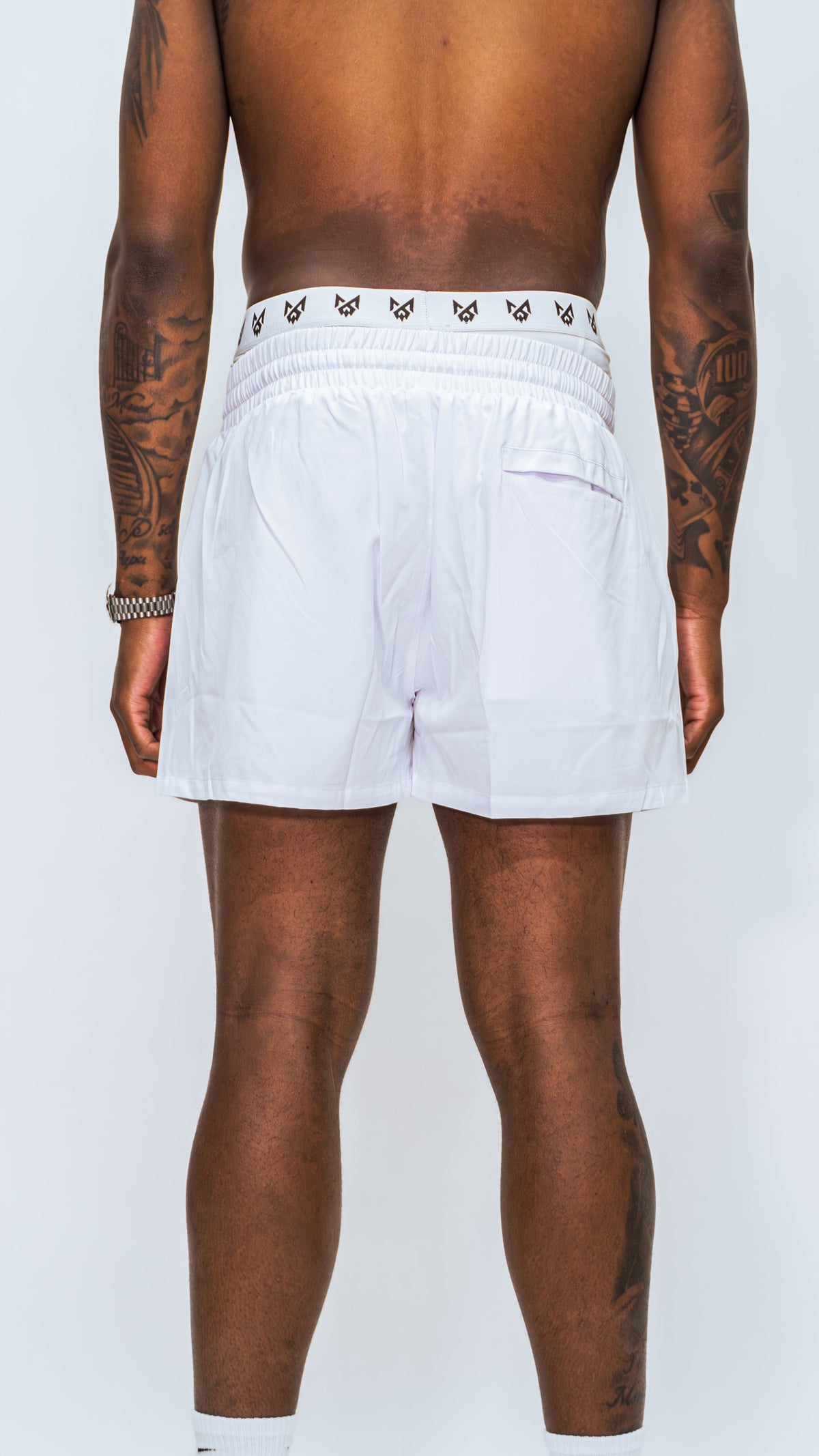 Rear view of model wearing Milkwhite short swim trunks, displaying rear pocket.