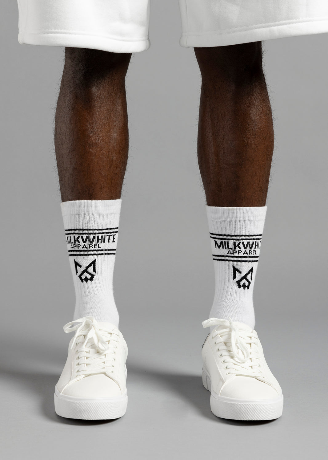 Front close-up of MilkWhite White Socks on a model, with black lettering and logos above white lace-up sneakers.