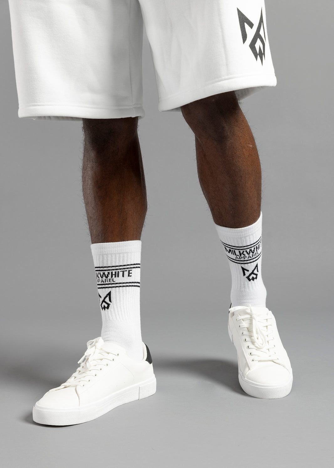 Close-up of MilkWhite White Socks worn with white sneakers, showing the black lettering, stripes and logo on the ribbed cuffs.