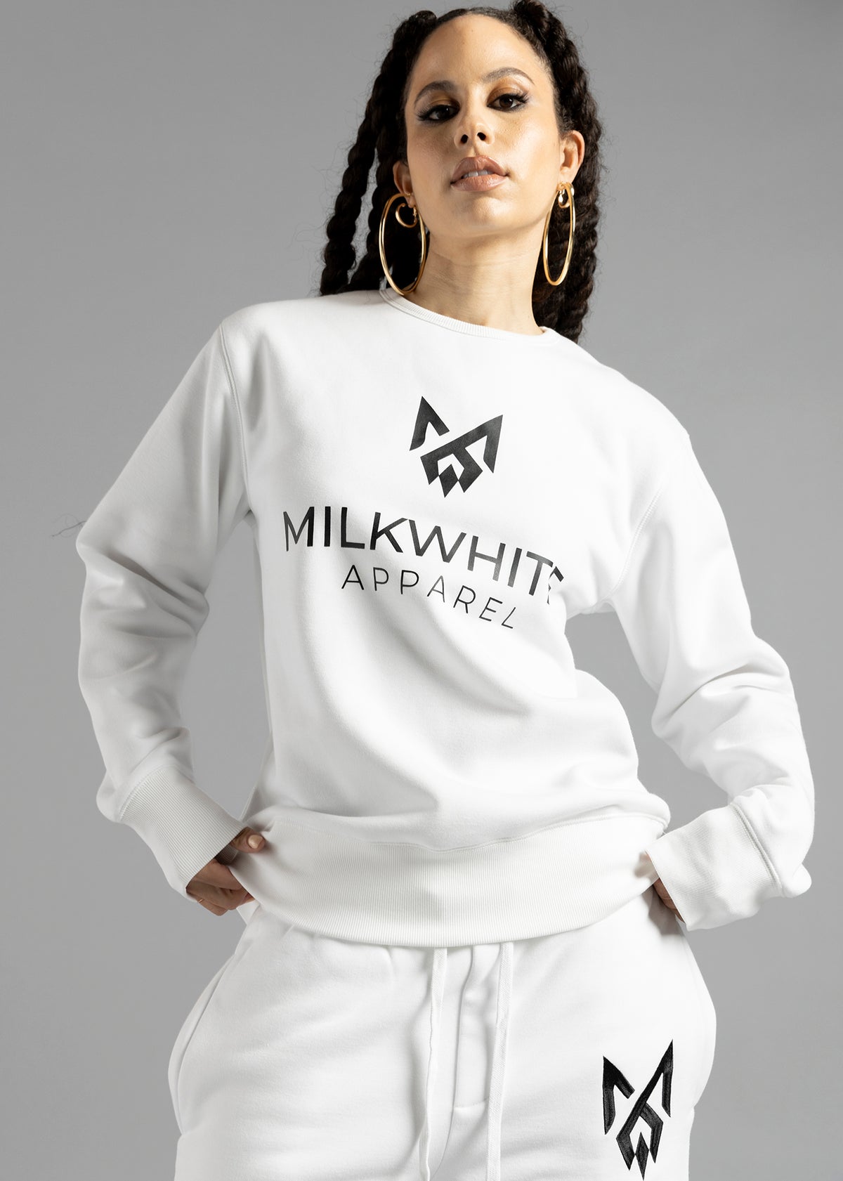 Front close-up of a model wearing the white Milk Essential Sweatshirt by MilkWhite, showing the dark chest logo, lettering and ribbed hem.