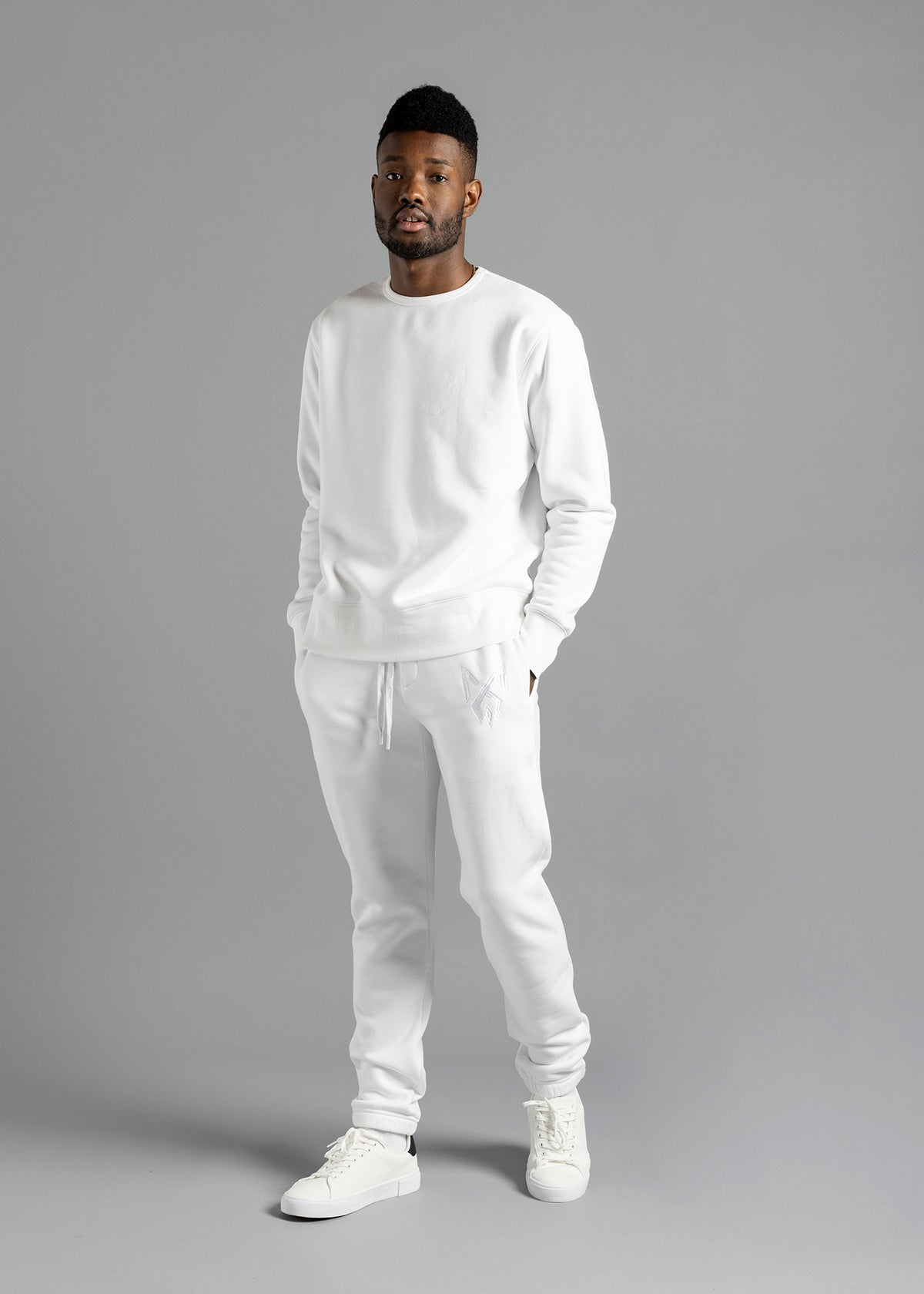 Full-length three-quarter front view of a model wearing the white Milk Essential Sweatshirt by MilkWhite, with hands in trouser pockets.