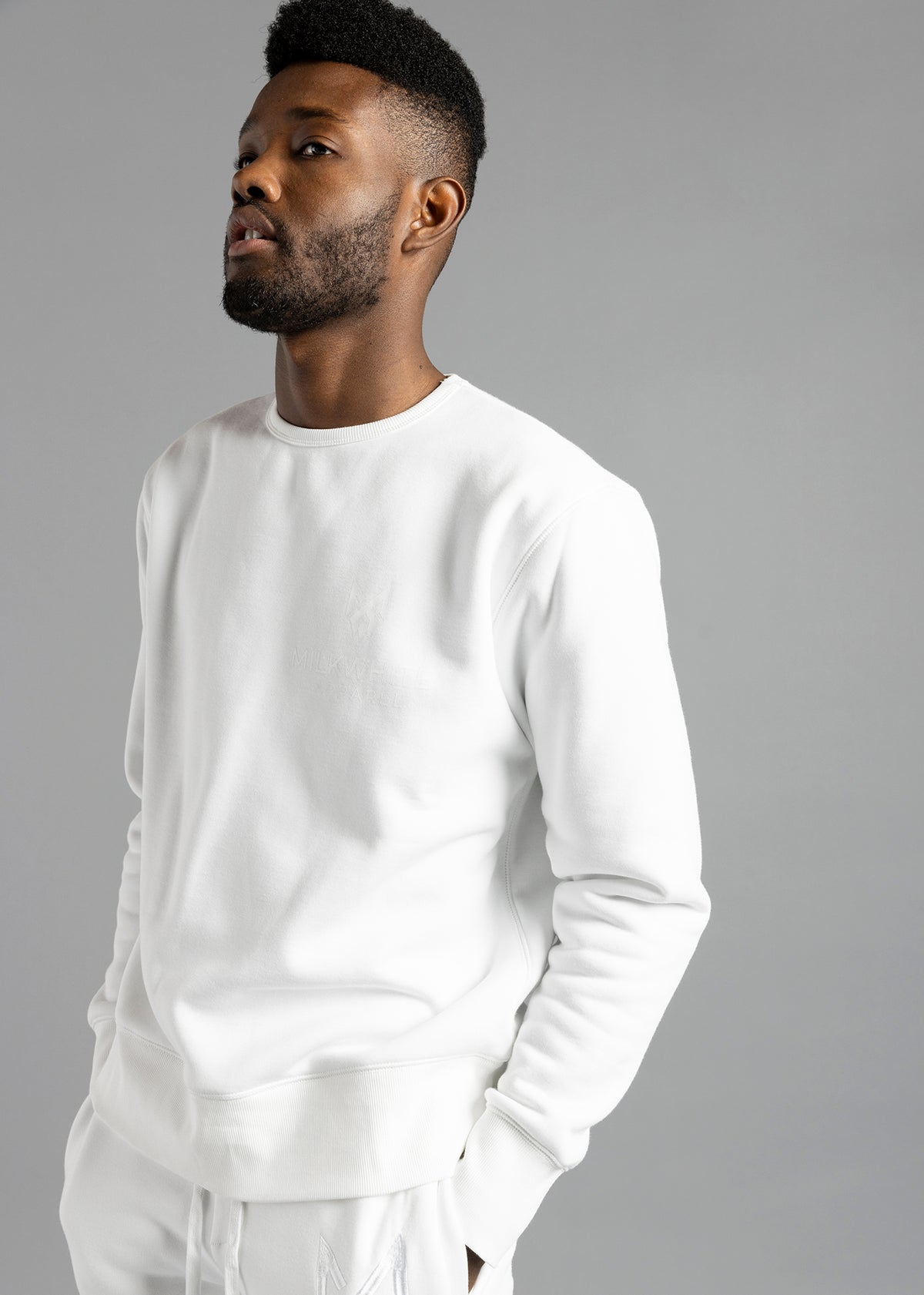 Three-quarter upper-body view of a model wearing the white Milk Essential Sweatshirt by MilkWhite, showing the crew neckline, long sleeves and ribbed hem.