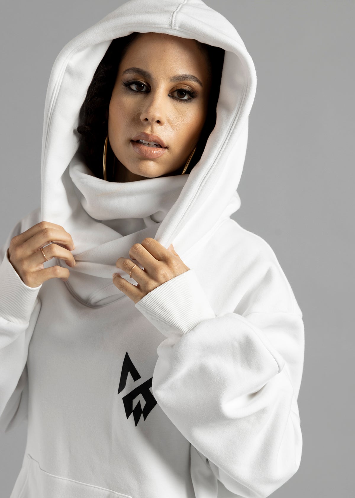 Front close-up of a model wearing the white Rosebud Hoodie by MilkWhite with the hood up and hands holding its edges.