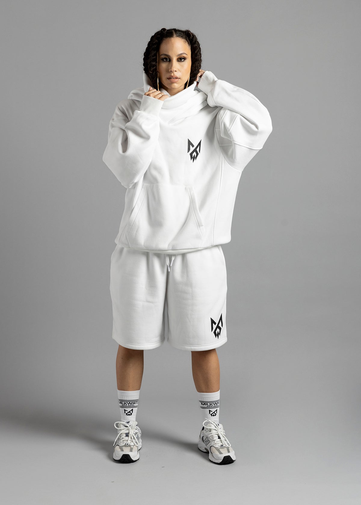 Full-length front view of a model wearing the white Rosebud Hoodie by MilkWhite, holding the draped neckline above the black chest logo.